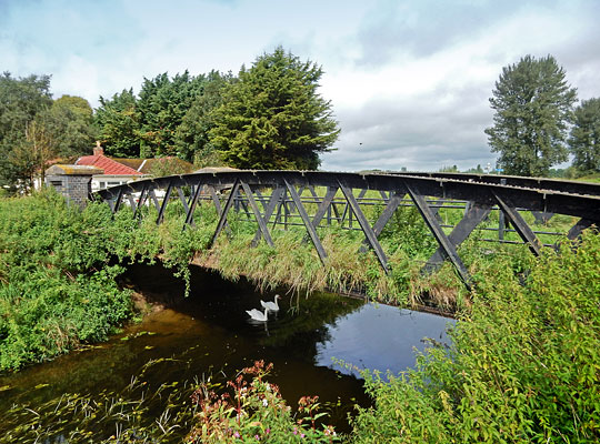 Built in 1903 to replace the original bridge, the structure comprises a pair of wrought iron ‘hogback’ trusses.