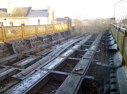 A recent view of the deck towards the site of the 23-arch approach viaduct. Note the waybeams that once carried the rails, the tops of the cast arches and the reverse sides of the dentils below the parapets. The upstanding brackets once carried wooden walkways for use by railway staff.