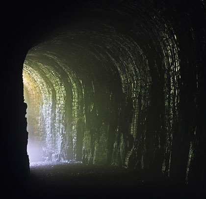 The tunnel's irregular profile is emphasised by light from the portal.