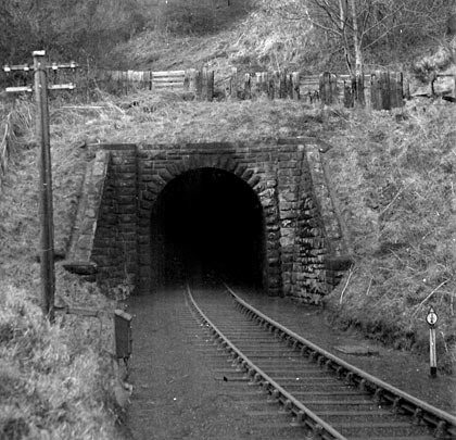 A milepost and telegraph pole stand sentinel in front of the tunnel's south portal, as the track enters on a curve.