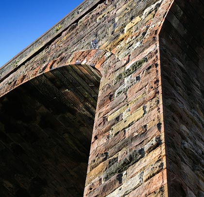 The piers, spandrels and parapets are formed of rockfaced rubble with red ashlar intrados.