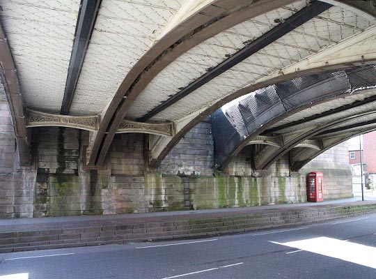 Looking south-west towards the former station, the gap between the pair of bridges to accommodate the island platform is clear. Also of note are the elegant bracing pieces between the arches, the dip in the road to allow double-decker trams and trolley buses to clear the bridge and the forlorn red telephone box.