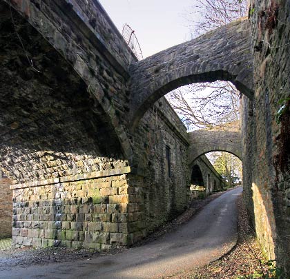 A lane runs beneath a pair of flying arches which separate the viaduct and an adjacent retaining wall.