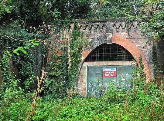 Paxton Tunnel's north portal is structurally assisted by large triangular wing walls parallel to the old trackbed, but all the brickwork is being lost to vegetation.