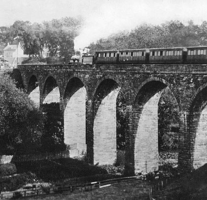 A passenger train trundles eastwards over the viaduct, approaching the adjacent station and tunnel.
