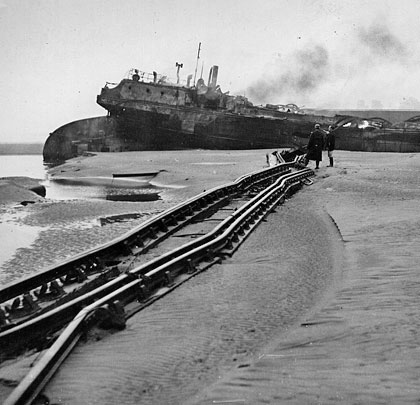 With the bridge's fallen rails in the foreground, one of the vessels involved sits marooned on a sand bank.