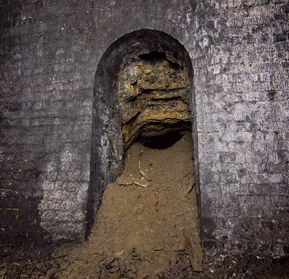 An archway cut in the sidewall - blocked by tipped spoil at the entrance - leads to a horizontal gallery.